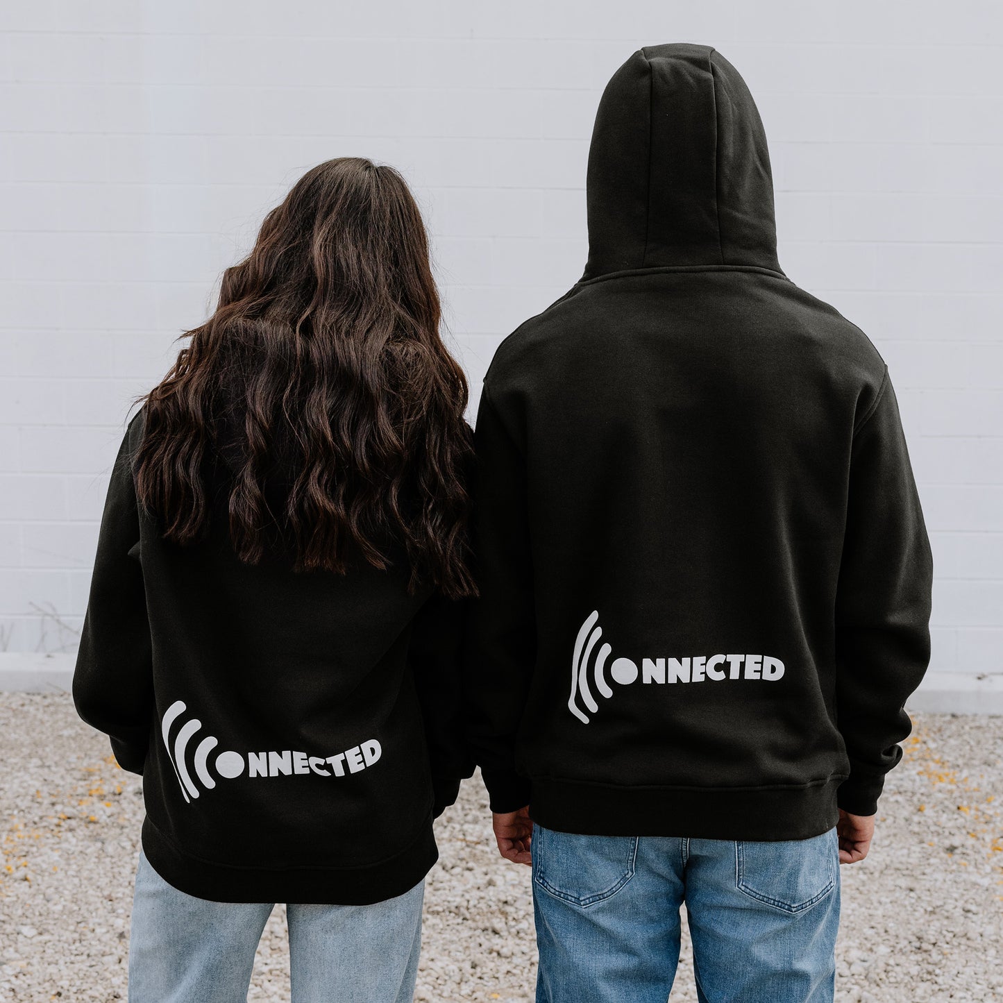 Couple in matching black OOsmash Connected hoodies showing WiFi signal design - stay connected together