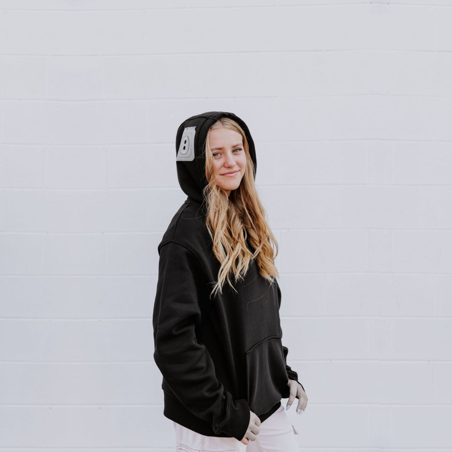 Model wearing OOsmash women’s black hoodie featuring gray plug accent and relaxed fit.