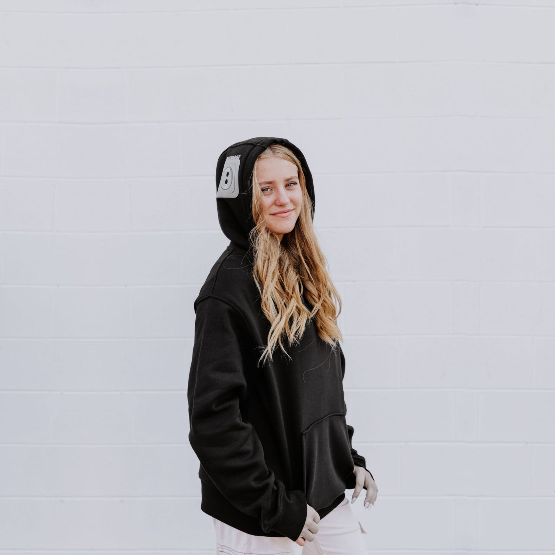 Model wearing OOsmash women’s black hoodie featuring gray plug accent and relaxed fit.